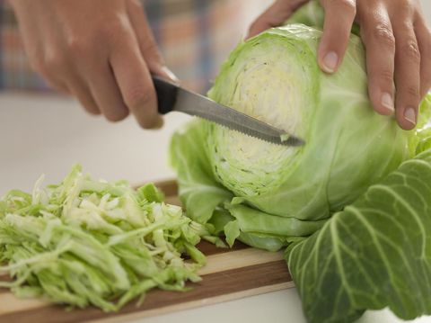 Woman cuts cabbage on cutting board in kitchen.