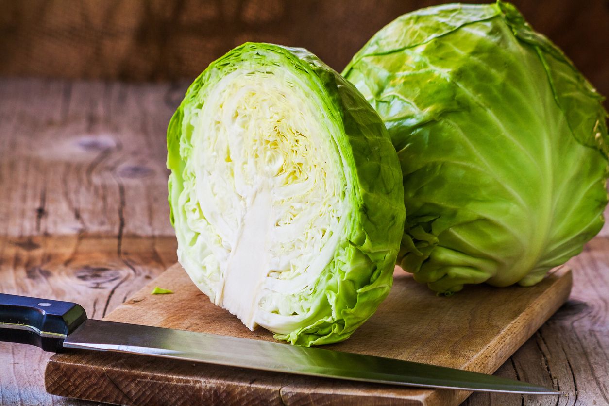 Fresh green cabbage cross section with water drops on rustic wooden cutting board, kitchen knife in foreground. Close up, selective focus