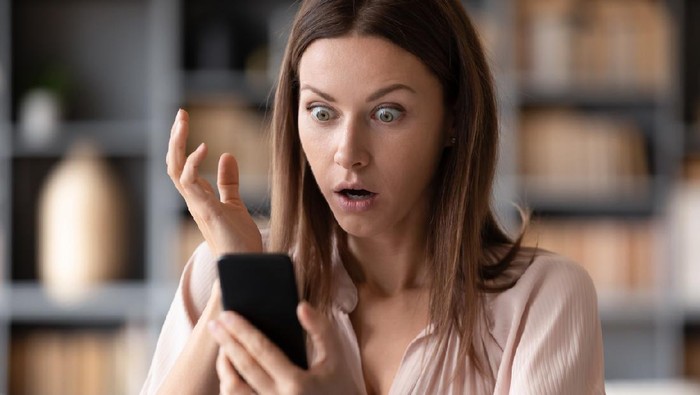 Head shot close up young shocked woman looking at mobile phone screen, received bank debt notification. Stunned frustrated lady reading sms with unbelievable news on smartphone, making big eyes.