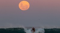 Indahnya bulan dipadu dengan para peselancar yang menaiki ombak menghasilkan gambar yang sempurna.