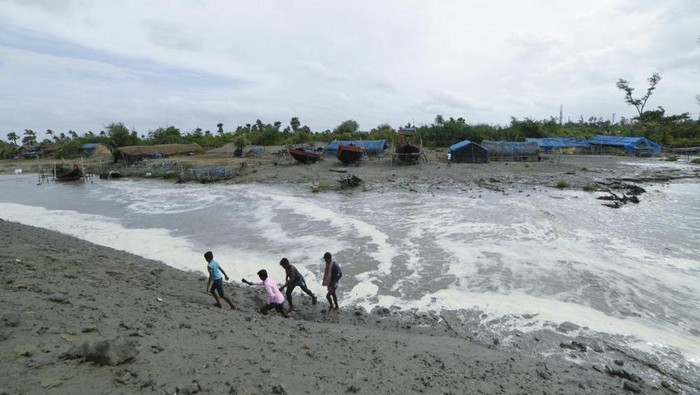 Village men walk past as sea water gushes in after breaking an embankment on the Bay of Bengal coast in South 24 parganas, West Bengal state, India, Tuesday, May 25, 2021. Tens of thousands of people are evacuating low-lying areas as Cyclone Yaas is expected to make landfall early Wednesday in Odisha and West Bengal states. (AP Photo/Mehaboob Uddin Gazi)