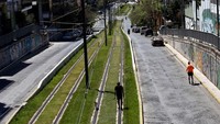 Seorang pria mengajak anjingnya berjalan-jalan di jalur trem di Athena, Yunani. Getty Images/Milos Bicanski  