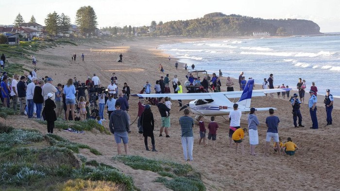 Spectators stand near a light plane that made an emergency landing on a beach in Sydney Wednesday, May 26, 2021. The recreational plane landed safely on a Sydney beach with three people aboard including a baby on Wednesday after its single engine failed, officials said. (AP Photo/Mark Baker)