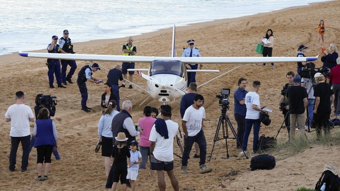 Mesin Rusak, Pesawat Ini Mendarat Darurat di Pantai Sydney Spectators stand near a light plane that made an emergency landing on a beach in Sydney Wednesday, May 26, 2021. The recreational plane landed safely on a Sydney beach with three people aboard including a baby on Wednesday after its single engine failed, officials said. (AP Photo/Mark Baker)
