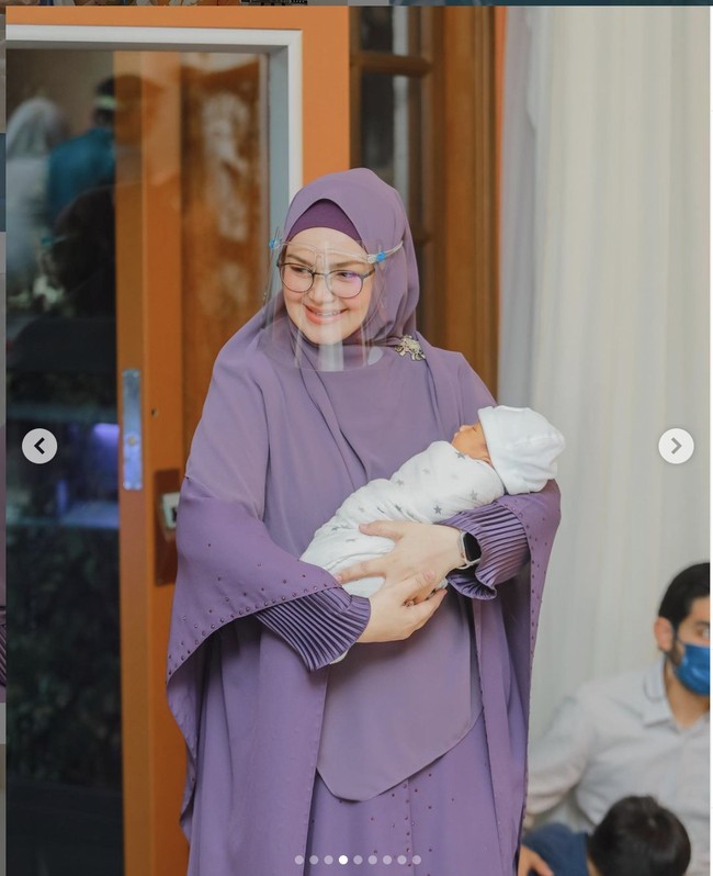 Saat acara akikah anaknya, pelantun Cindai itu tampil dengan busana muslim ungu rancangan Shanel Harun. Siti tampak mengenakan face shield sebagai upaya mematuhi protokol kesehatan pencegahan COVID-19. Foto: Dok. Instagram@ ctdk