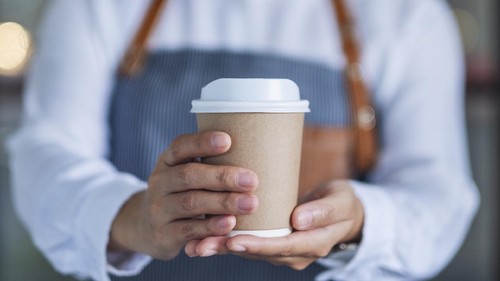 A waitress holding and serving a paper cup of hot coffee in cafe