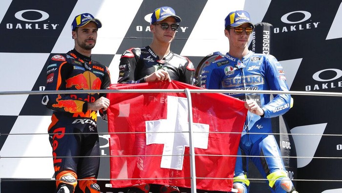 From left, second placed KTM rider Miguel Oliveira, of Portugal, first placed, Yamaha rider Fabio Quartararo, of France, and third placed Suzuki rider Joan Mir, of Spain, hold the Swiss flag to honor 19 years-old Swiss rider Jason Dupasquier, during the podium ceremony at the end of the Motogp Grand Prix of Italy at the Mugello circuit, in Scarperia, Italy, Sunday, May 30, 2021. Dupasquier died Sunday after being hospitalized Saturday, at the Florence hospital, following his crash during the qualifying practices of the Moto3. (AP Photo/Antonio Calanni)