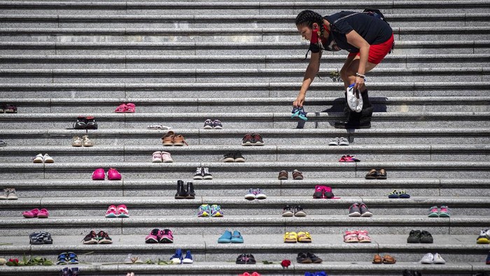 Lorelei Williams places one of 215 pairs of childrens shoes on the steps of the Vancouver Art Gallery as a memorial to the 215 children whose remains have been found buried at the site of a former residential school in Kamloops,  in Vancouver, British Columbia, Canada on Friday, May 28, 2021. Chief Rosanne Casimir of the Tkemlups te Secwépemc First Nation said in a news release Thursday that the remains were confirmed last weekend with the help of a ground-penetrating radar specialist.  (Darryl Dyck/The Canadian Press via AP)