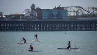 Orang-orang melakukan olahraga dayung dengan latar belakang Dermaga Istana Brighton, Inggris.  
