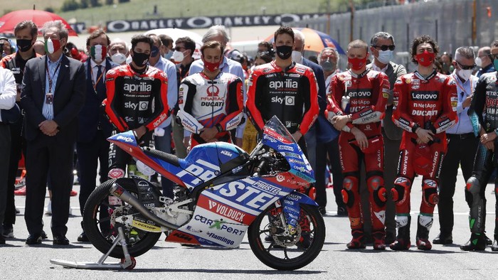 Penghormatan untuk Rider Moto3 Jason Dupasquier Teammates of 19 years-old Swiss pilot Jason Dupasquier stand near his motorbike, right, as they pay a minute of silence in his memory prior to the start of the Motogp Grand Prix of Italy at the Mugello circuit, in Scarperia, Italy, Sunday, May 30, 2021. Dupasquier died Sunday after being hospitalized Saturday, at the Florence hospital following his crash during the qualifying practices of the Moto3. (AP Photo/Antonio Calanni)