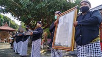 Di sisi timur halaman Istana Gebang, berdiri beberapa lelaki berpakaian beskap dengan membawa foto Presiden Soekarno, patung Garuda Pancasila, dua kotak kayu hitam pekat yang berisi teks pidato BK di BPUPKI, bendera merah putih dan teks Pancasila.