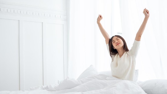 Asian woman wake up in the morning, sitting on white bed and stretching, feeling happy and fresh