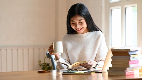 Woman reading book and holding her coffee in home office.