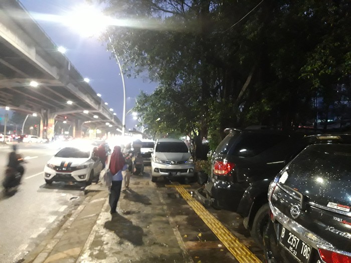 Mobil parkir di trotoar depan Halte TransJakarta Kayu Putih Rawasari, Jakarta Pusat saat malam hari.