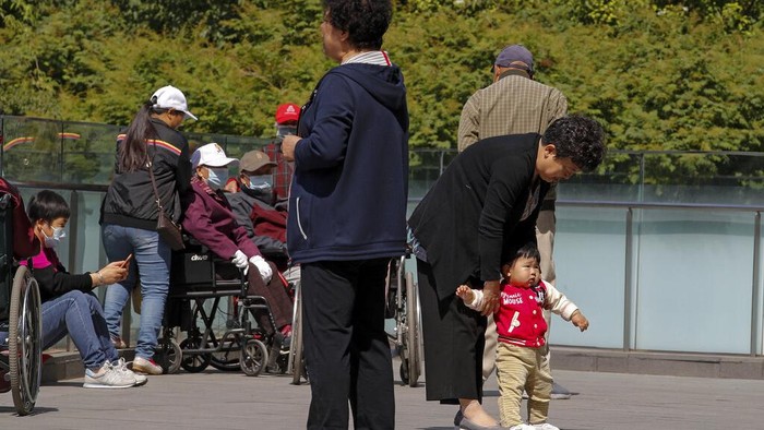 A woman plays with a child in a compound near a commercial office building in Beijing on May 10, 2021. Chinas ruling Communist Party will ease birth limits to allow all couples to have three children instead of two to cope with the rapid rise in the average age of its population, a state news agency said Monday. (AP Photo/Andy Wong)