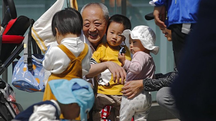 A woman plays with a child in a compound near a commercial office building in Beijing on May 10, 2021. China's ruling Communist Party will ease birth limits to allow all couples to have three children instead of two to cope with the rapid rise in the average age of its population, a state news agency said Monday. (AP Photo/Andy Wong)
