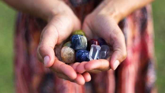 A young woman carefully holds a selection of vibrant gemstones as they reflect the soft sunlight.
