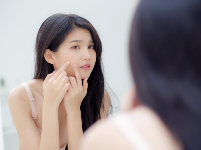 Beautiful young asian woman looking the mirror and touch face is a acne, zit treatment, beauty girl problem beauty and skin with wrinkled on facial in the room at home, makeup and cosmetic concept.