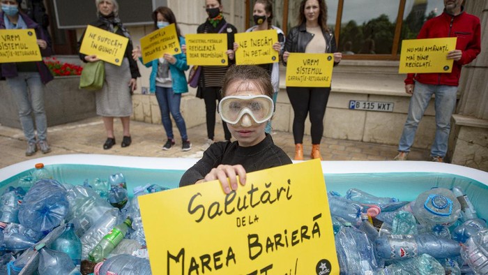 An activist lies in an inflatable pool filled with PET plastic bottles during a protest outside the environment ministry demanding the introduction of the deposit refund scheme that will stimulate the population to recycle in Bucharest, Romania, Thursday, June 3, 2021. Romania has the second lowest rate of recycling in the European Union with just 11 percent of the waste being recycled, compared to the block's average of 47 percent. (AP Photo/Alexandru Dobre)