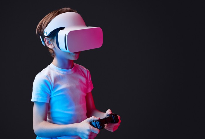 Kid wearing VR glasses and playing videogame illuminated with neon lights on black backdrop