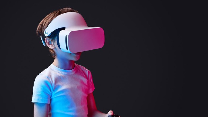 Kid wearing VR glasses and playing videogame illuminated with neon lights on black backdrop