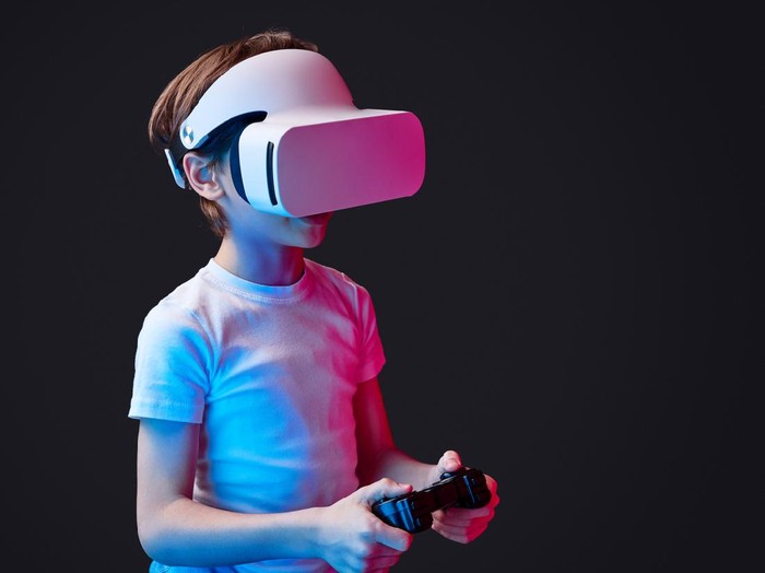 Kid wearing VR glasses and playing videogame illuminated with neon lights on black backdrop