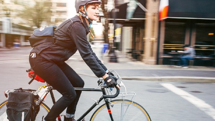 A smiling young woman commuting in an urban city environment on her street bicycle, waterproof panniers on her bike rack.  She rides the streets of downtown Portland, Oregon.  Intentional motion blur.