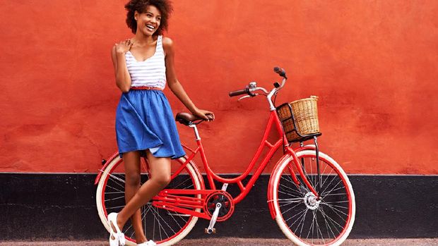 Young smiling woman standing in front of an orange wall with her bicycle
