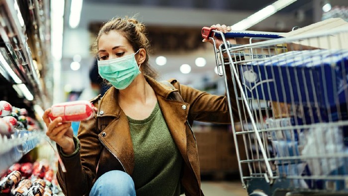 1215276675 Young woman wearing protective mask and buying food in grocery store during coronavirus pandemic.