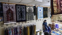 Seorang pedagang menunggu pembeli dengan duduk di sekitar deretan perlengkapan untuk beribadah.
