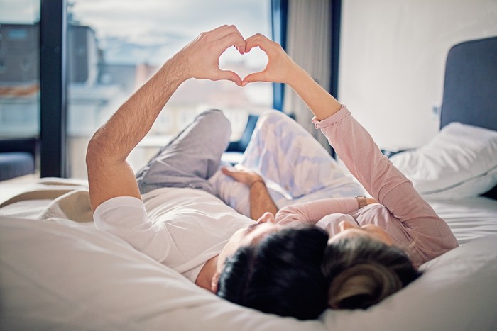 Ilustrasi Seks Couple is lying on the bed and making heart with their hands