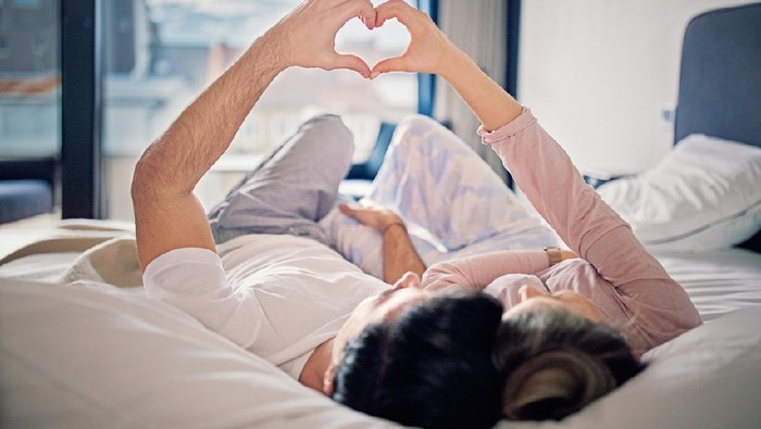 Couple is lying on the bed and making heart with their hands