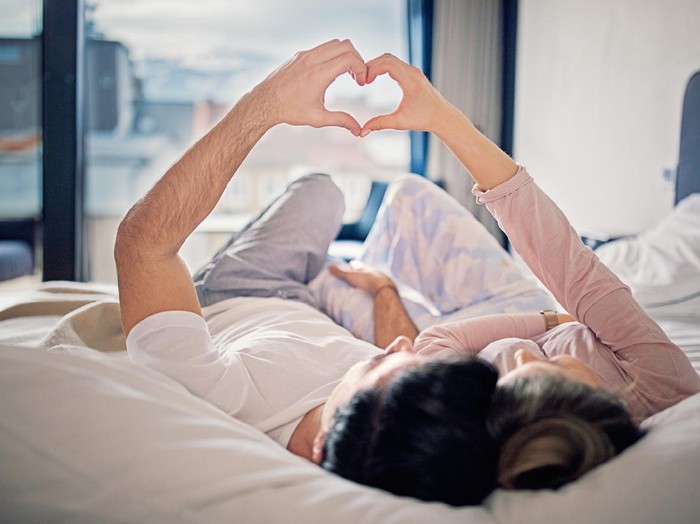 Couple is lying on the bed and making heart with their hands