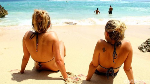 Ilustrasi wisatawan di pantai bali, berjermur, menikmati pantai.