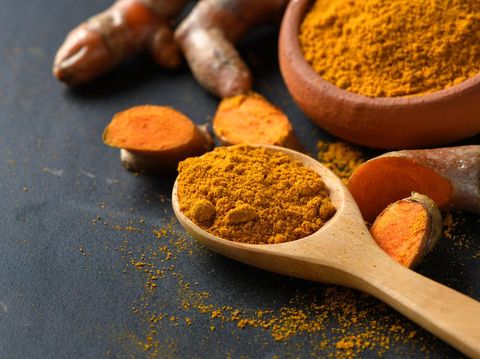 turmeric powder in wood spoon on black table, spices and herb concept
