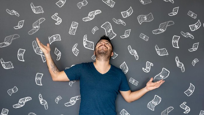 Excited man under a shower of money with bills floating in the air - economy concepts