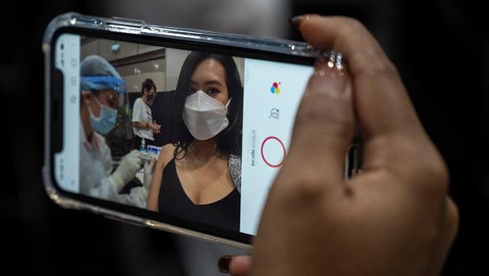 BANGKOK, THAILAND - JUNE 07: A woman takes a selfie while being administered the AstraZeneca Covid-19 coronavirus vaccine by a health worker at the mass vaccination site inside the Siam Paragon shopping mall on June 07, 2021 in Bangkok, Thailand. Thailand began rolling out its long-anticipated mass vaccination program on Monday. The government has said it will vaccinate around 70 percent of its population by the end of the year, with either Sinovac or AstraZeneca vaccines. The government has also announced plans to acquire Pfizer and Johnson & Johnson vaccines to bolster its program. (Photo by Sirachai Arunrugstichai/Getty Images)