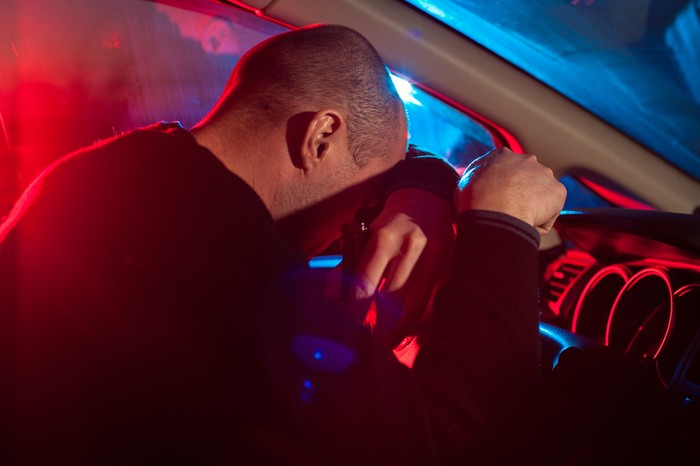 638093310 Upset drunk driver is caught driving under alcohol influence. Man covering his face from police car light.