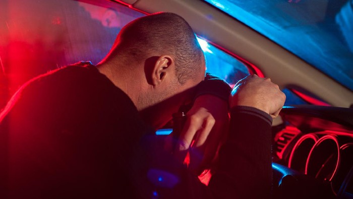 638093310 Upset drunk driver is caught driving under alcohol influence. Man covering his face from police car light.