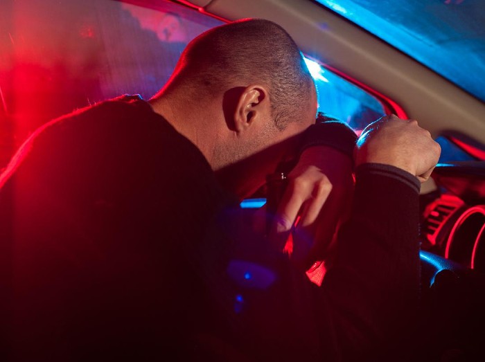 638093310 Upset drunk driver is caught driving under alcohol influence. Man covering his face from police car light.