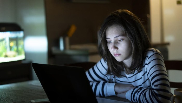 Young girl is reading alone on her laptop late at night