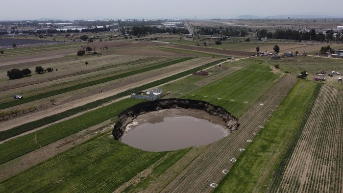 Sinkhole di Meksiko Terus Menelan Lahan Pertanian Warga With the Iztaccíhuatl volcano in the background, security tape bars access in the perimeter around a water filled sinkhole in Zacatapec, on the outskirts of Puebla, Mexico, Wednesday, June 9, 2021. The massive water-filled sinkhole continues swallowing farmers' fields in the central Mexican state of Puebla. (AP Photo/Fernando Llano)
