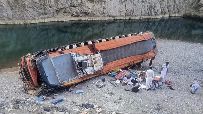Locals gather supplies next to a damage bus at the site of accident in Khuzdar, a remote district in the Pakistans southwestern Baluchistan province, Friday, June 11, 2021. The bus carrying pilgrims overturned on a highway and fell into the ravine before dawn on Friday, killing more than a dozen and injuring scores of people, police and officials said. (AP Photo/Younis Baloch)