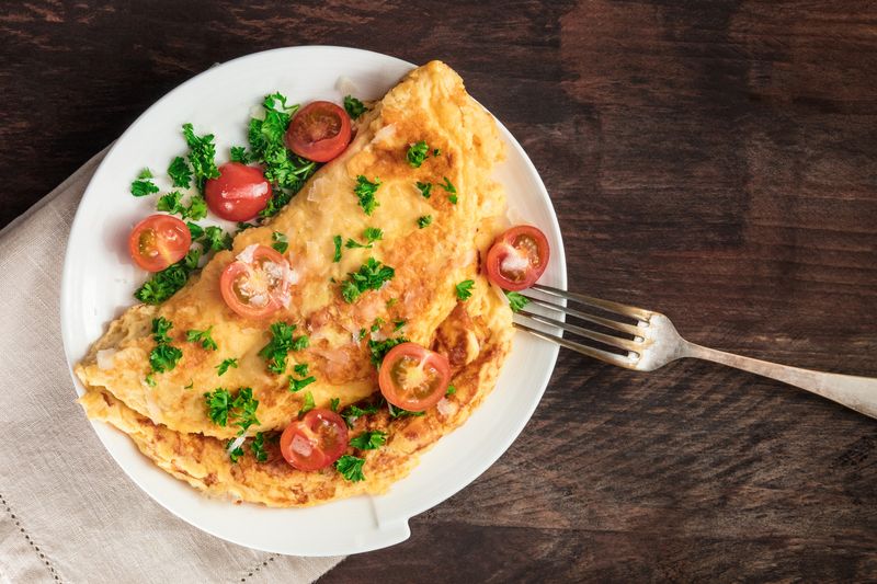 Omelet A photo of an omelette with cherry tomatoes, parsley. and grated cheese, shot from above on a rustic wooden texture with a place for text