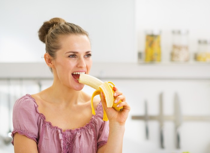 Wanita makan pisang Young woman eating banana in kitchen