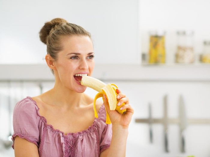 Young woman eating banana in kitchen