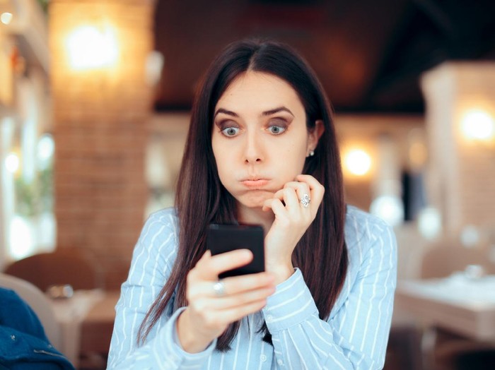 1029635472 Stressed young woman checking her phone in a restaurant