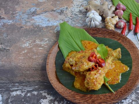 Ayam Kalio Padang or wet saucy chicken rendang. Served on banana leaf and turmeric leaf garnish with chili and kaffir lime leaf