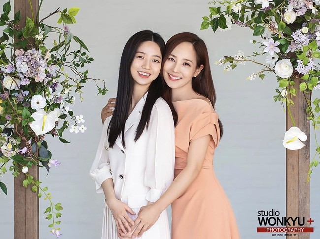 Mereka pun berpose di antara dekor bunga. Eugene memeluk Kim Hyun Soo dari belakang, dan memegang tangannya. Ia mengenakan dress off shoulder berwarna peach, sementara putrinya mengenakan blazer dan rok putih. Foto: dok. Instagram studiowonkyu