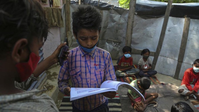 Kala Anak-anak Pemukiman Kumuh di India Ikut Kelas Online A teacher gestures as children wearing face masks as a precaution against the coronavirus attend online classes at a slum on the outskirts of Jammu, India, Monday, June 14, 2021. (AP Photo/Channi Anand)